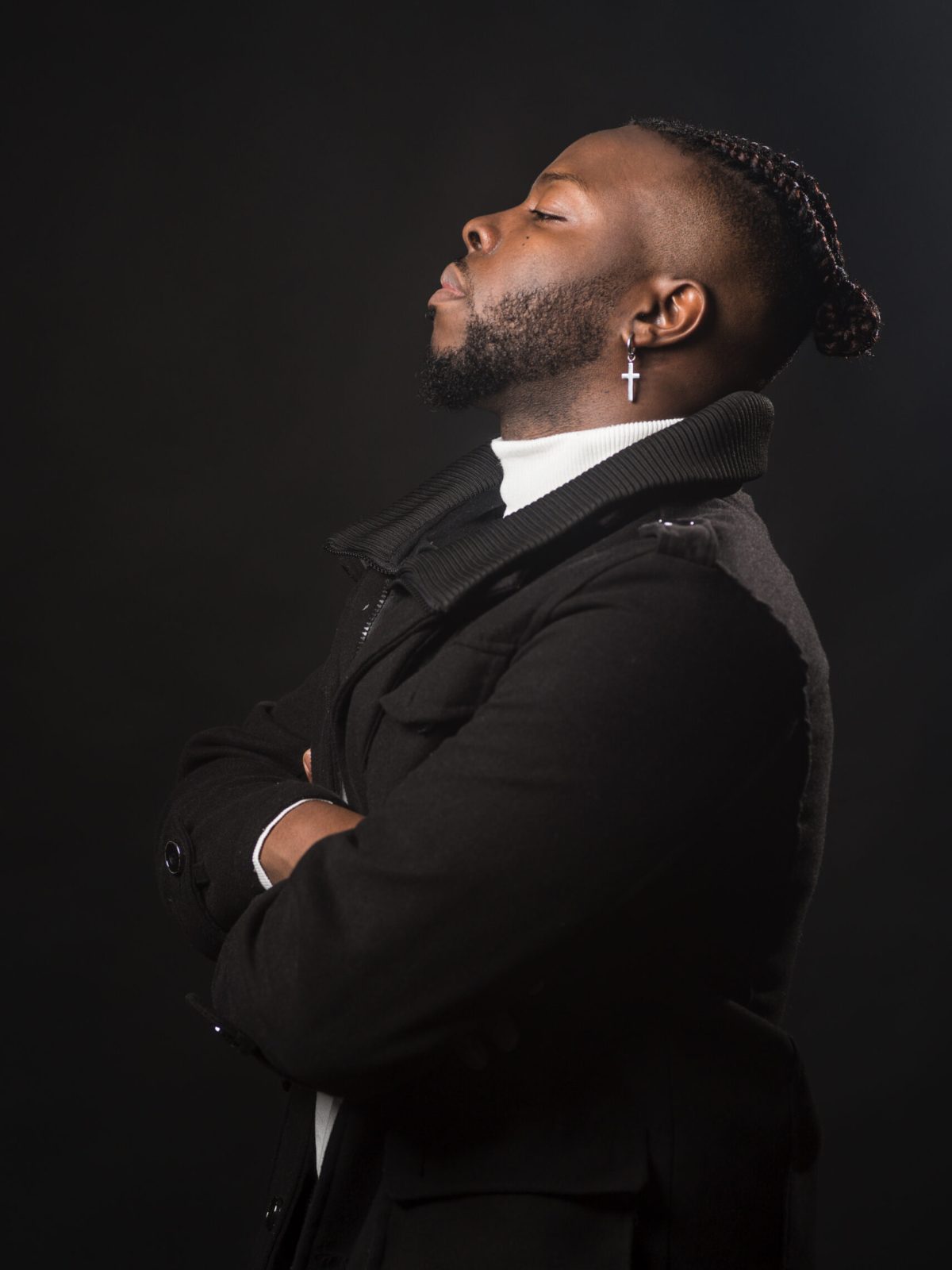Black man in profile, very serious and with his arms crossed. Mid shot. Black background.