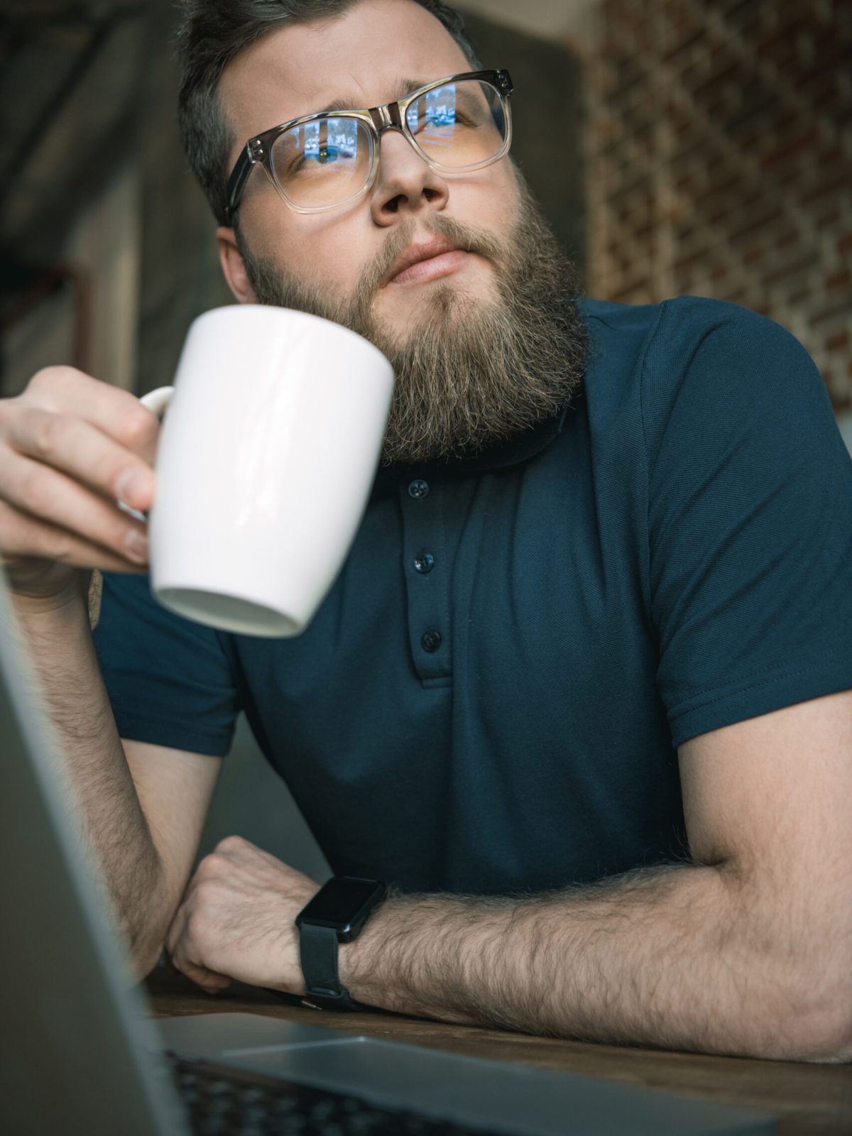 young bearded man in glasses drinking coffee while sitting at table